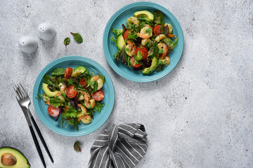 Green mix salad with tomatoes and shrimp and sauce on a concrete background. View from above