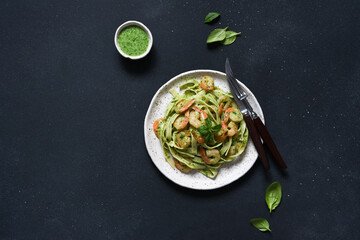 Pasta with pesto and shrimp on a plate on the kitchen table, top view
