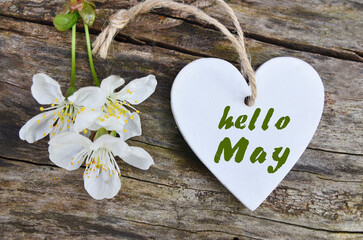 Hello May greeting card with decorative white heart and cherry flowers on a wooden background. Springtime concept.Selective focus.