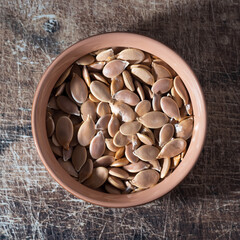 Pumpkin seeds on a clay plate on a brown scratched board. Texture of nuts on a wooden old table. Lots of nuts in a pile.