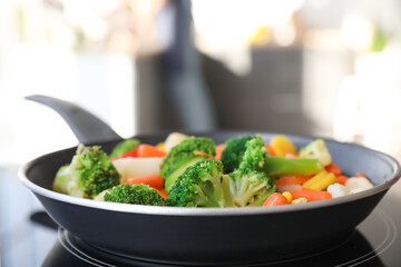 Frying pan with vegetables on electric stove in kitchen, closeup