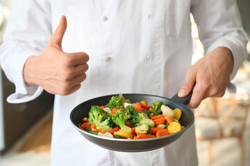 Male chef with fried vegetables showing thumb-up in kitchen, closeup
