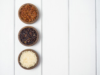 Three types of rice in wooden bowls on a white wooden table. red ,black and white rice ,copy space