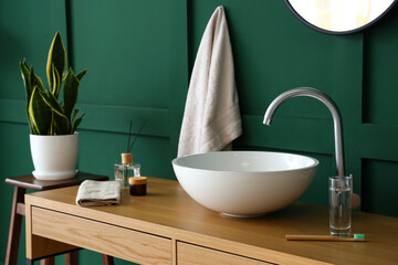 Fototapeta na wymiar Table with sink and bath supplies near green wall
