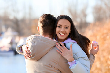 Happy young woman with engagement ring hugging her fiance after marriage proposal near river