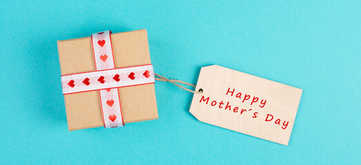Small gift box with a heart ribbon on a blue colored background, happy mothers day present