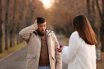 Young woman proposing to her shocked boyfriend in park