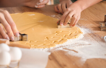 Mature woman cutting dough for cookies at table in kitchen, closeup