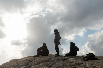 Three male hiking friends enjoying a scenic view at the peak of a mountain on a cloudy day in Spain