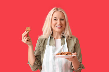 Mature woman holding plate with cookies on red background