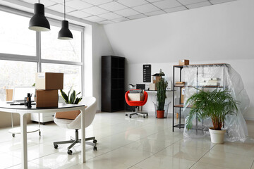 Cardboard boxes with belongings and furniture in interior of office on moving day