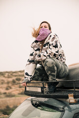 Woman on the top of a car wearing camouflage clothes and a violet bandana