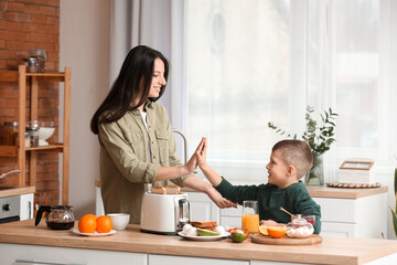 Little boy and his mother giving each other high-five while making tasty toasts in kitchen