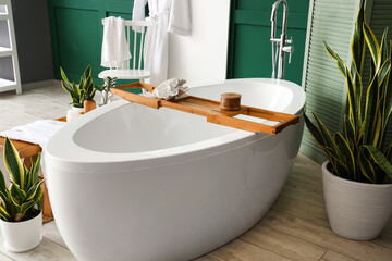 Wooden tray with jar and decor on white bathtub in room