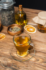 glass cup of tea near blurred jars on wooden surface isolated on black.