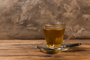 Cup of tea on saucer and spoon on wooden surface on textured stone background.