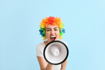 Funny young woman in colorful wig and with megaphone on blue background. April fools' day...