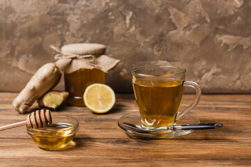 Tea and honey in bowl on wooden surface on textured stone background.