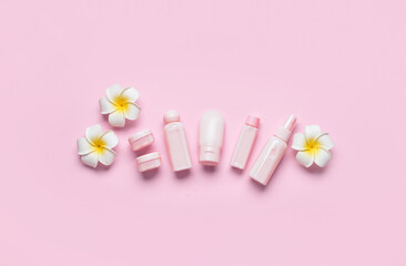 Travel bottles, jars with cosmetic products and flowers on pink background
