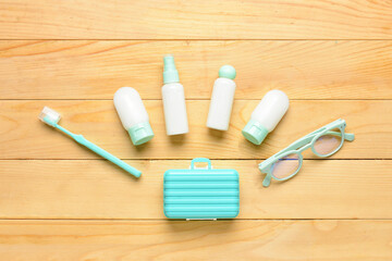 Travel bottles with cosmetic products, eyeglasses and toothbrush on wooden background