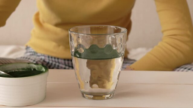 Girl putting a spoon of chlorella algae powder into a glass of water and stirring it