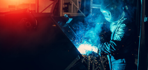 Industrial steel welder in process of work in metal factory. Sparks and smoke fly from welding. Horizontal banner image with copy space - obrazy, fototapety, plakaty