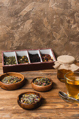 Dry tea, cup and jar with honey on wooden surface on textured stone background.