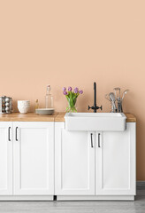 White counters with sink, tulips in vase and kitchen utensils near beige wall