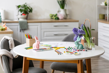 Easter bunnies with paints and supplies on table in kitchen