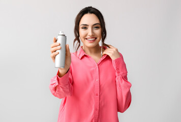 Pretty young woman with hair spray on grey background