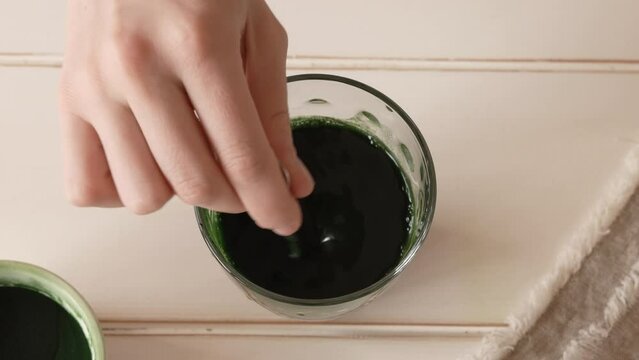 Hand stirring chlorella algae powder in a glass of water, top view