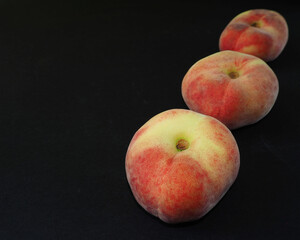 close-up of three fig peaches on a black background. side view