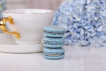 Cup of tea, sweet macaroons and hydrangea flower on blue background

