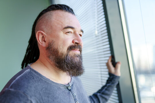 Man looking out the window. Portrait of an adult man with a mohawk and dreadlocks. A middle-aged man with a beard and an unusual hairstyle