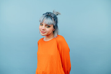 Beautiful girl in orange clothes and with blue hair stands on a colored background and looks at the camera with a smile on his face.