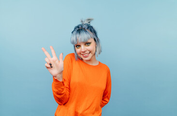 Positive lady with blue hair standing on a blue background dressed in an orange sweater and showing...