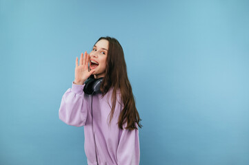 Positive woman in a purple sweatshirt stands against a blue background and looks at the camera with a smile on his face.