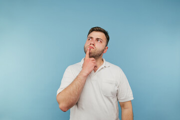 Portrait of an adult man with a beard in a white T-shirt on a blue background, pensive looking aside at copy space