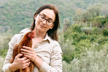 Woman holding brown hen in her hands in the farm. Free-grazing domestic hen on a traditional free range poultry organic farm.