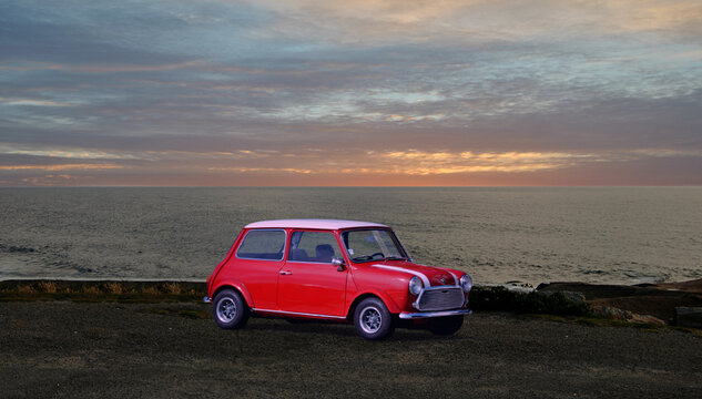 Carro antigo de marca inglesa, vermelho e branco estacionado &agrave; beira mar ao fim da tarde com por do sol