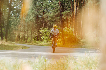 Male professional cyclist trains on a forest asphalt road. . Cycling in the woods. Professional cyclist trains outside the city, photo in orange tones