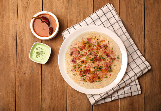 Top view of an Uttapam Dosa Indian dish, Hot sauce and small Salad dressing dish on a wooden table