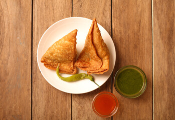 Top view of fried Samosa with pickled pepper, green sauce and red sauce on a wooden table