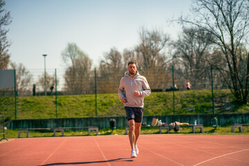 Obraz premium A man in a gray hoodie is jogging at a sports stadium.