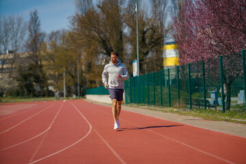 Obraz premium A man in a gray hoodie is jogging at a sports stadium.
