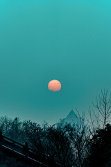 Vertical shot of a full moon in the teal sky above the leafless trees