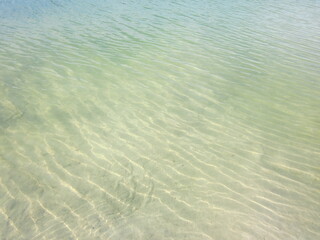 Shallow waves on the beach with translucent clean sand, in green-yellow tones. A ripple of waves with transparent reflexes and shadows