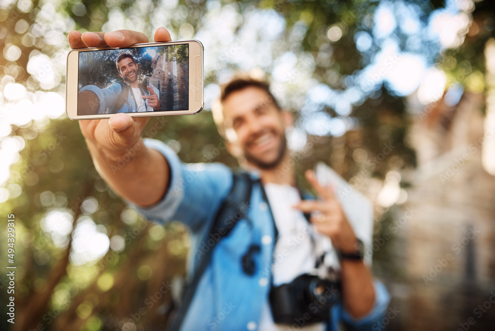 Wall mural Making sure hes in the pictures. Cropped shot of a handsome young man taking selfies on his mobile phone while on vacation.