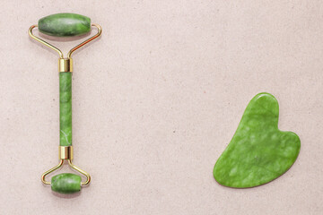 Facial massage jade gouache scraper and face roller on abstract paper background.