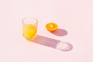 A glass of orange juice with a slice of orange on a pink background. Minimal aesthetic beverage concept.